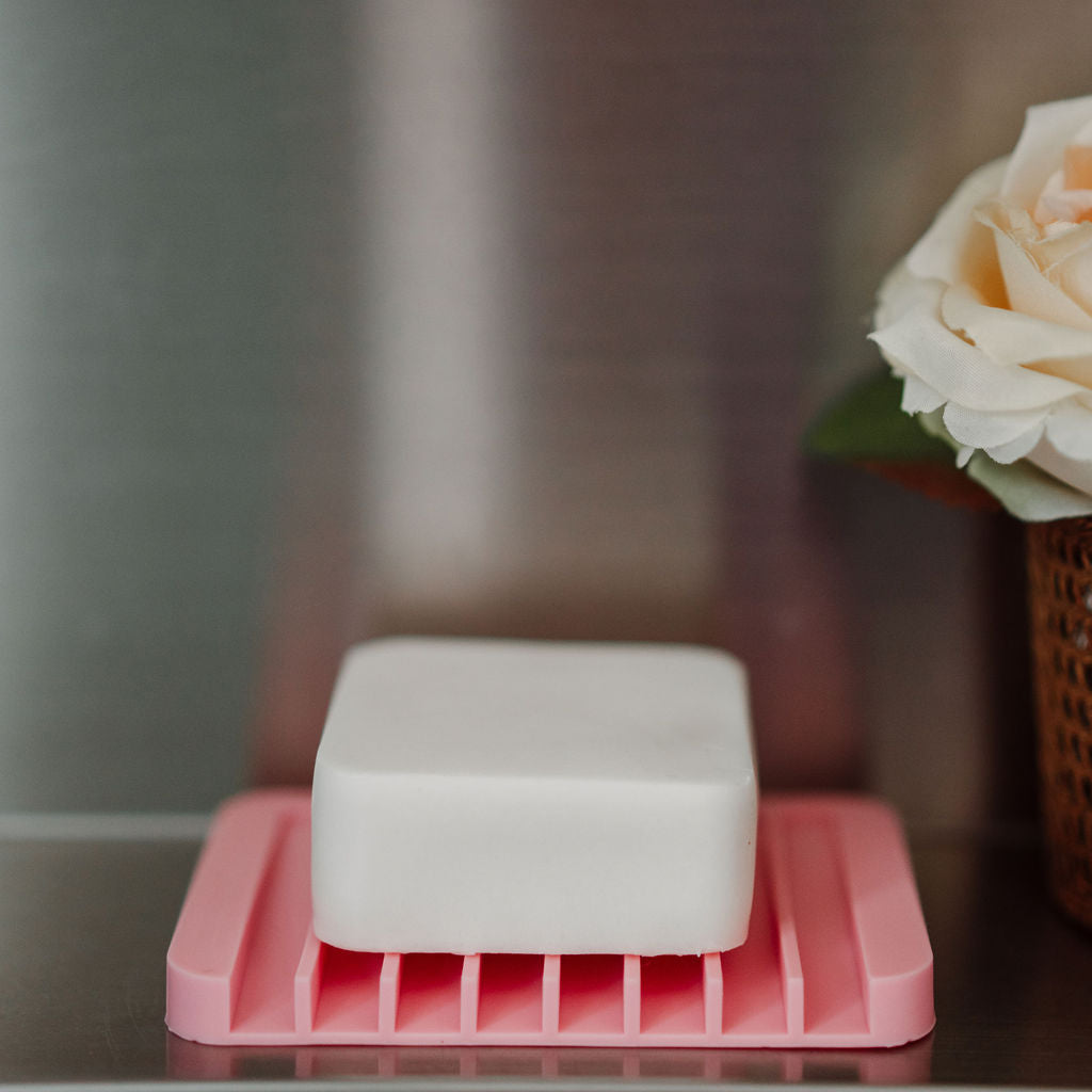 Bar of soap on a pink soap dish with a blurred background