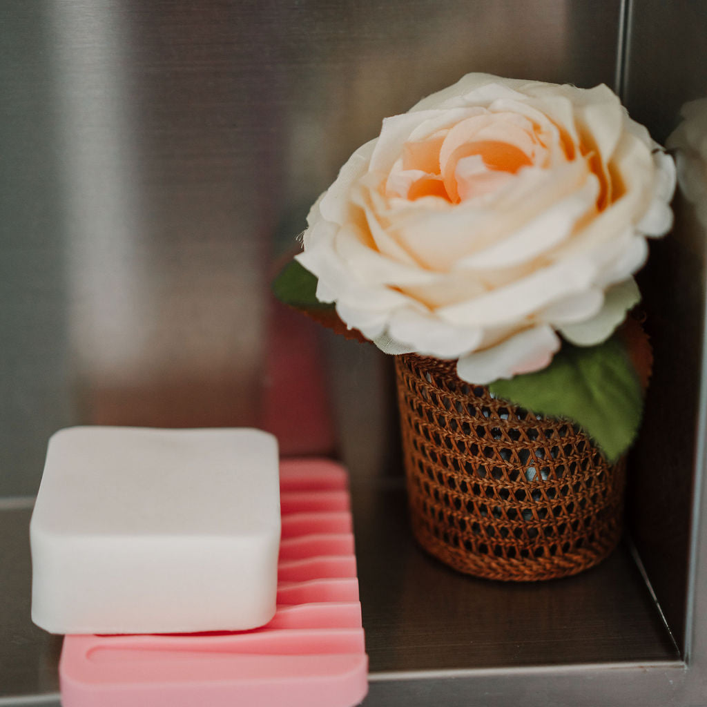 Stack of pink and white soap bars with a white rose in a brown pot on a metallic surface.