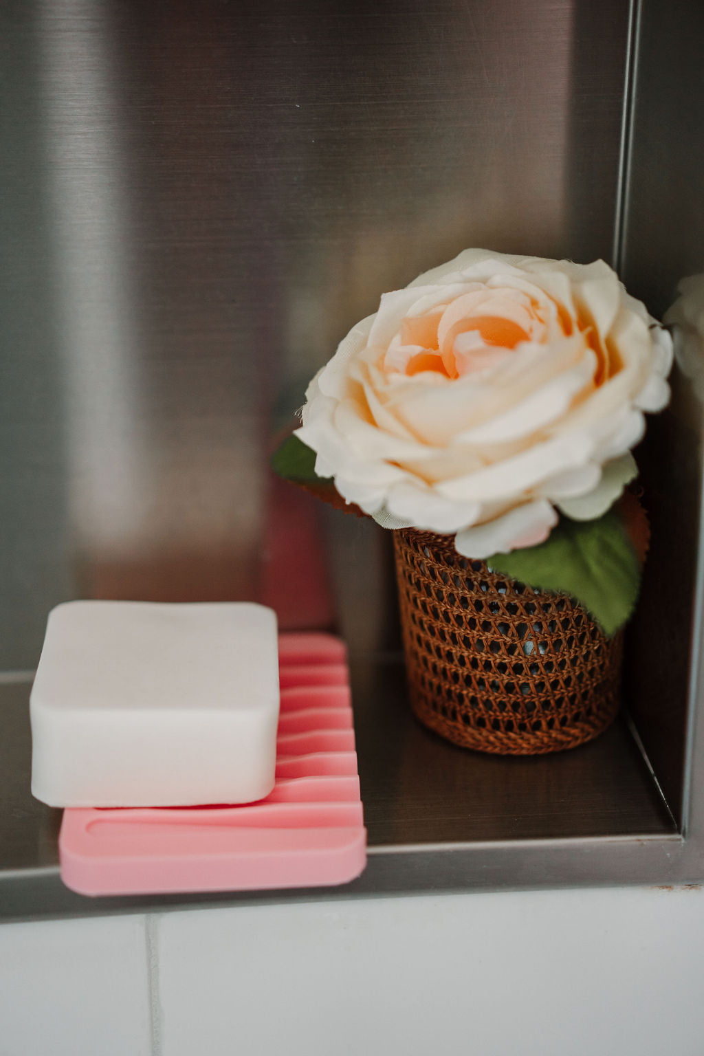 Stack of pink and white soap bars with a white rose in a brown pot on a metallic surface.