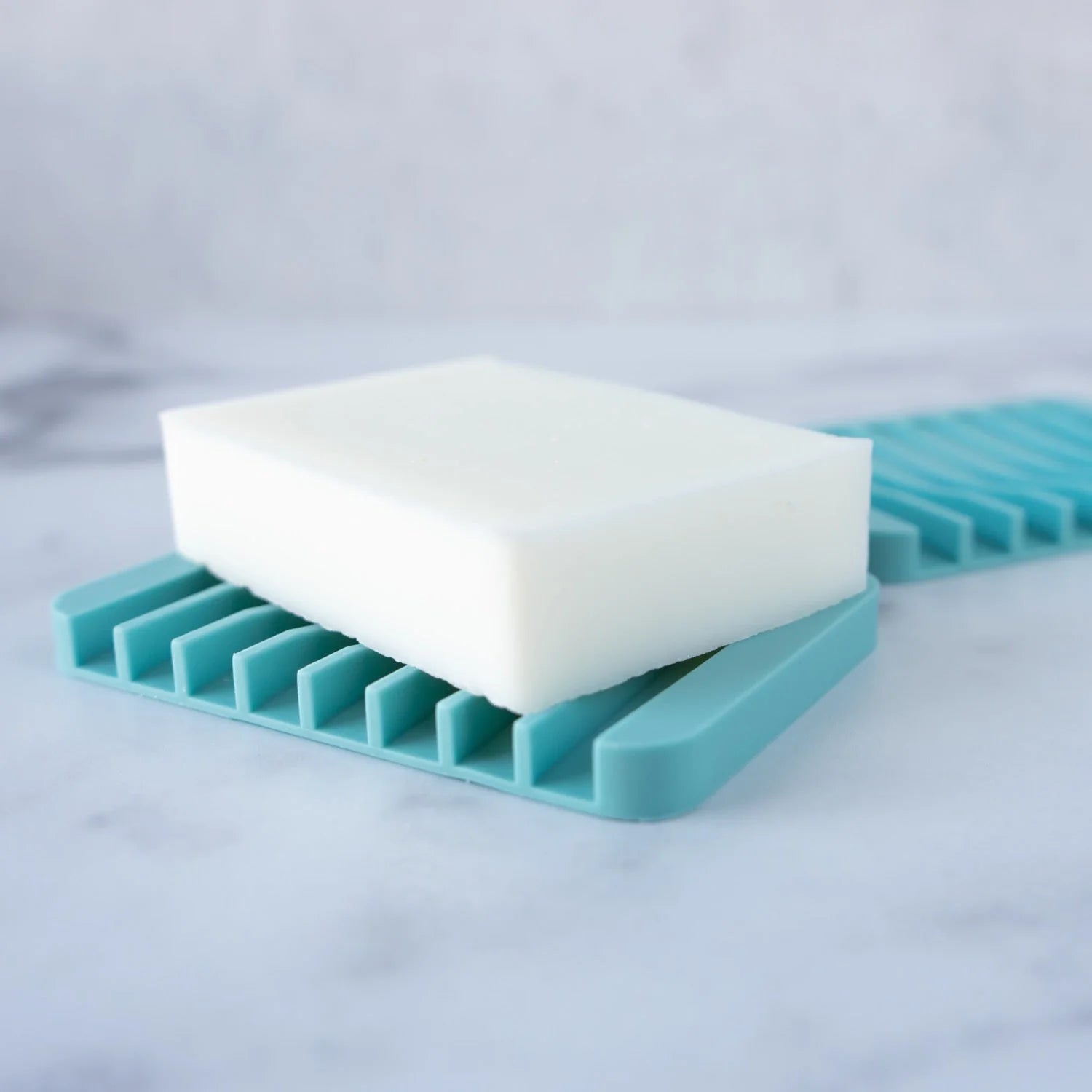 A blue silicone soap dish with a bar of soap on a marble surface.