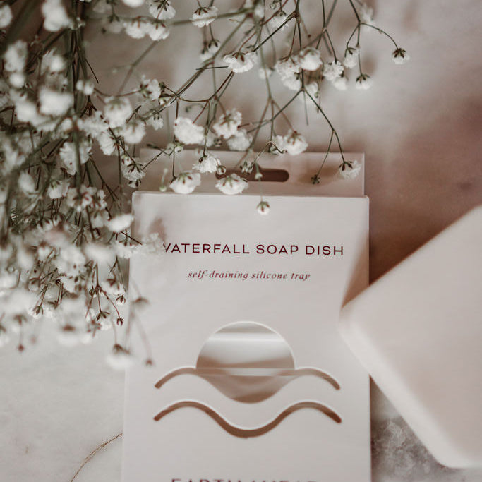 Earth Ahead soap dish with a bar of soap and white flowers on a marble surface