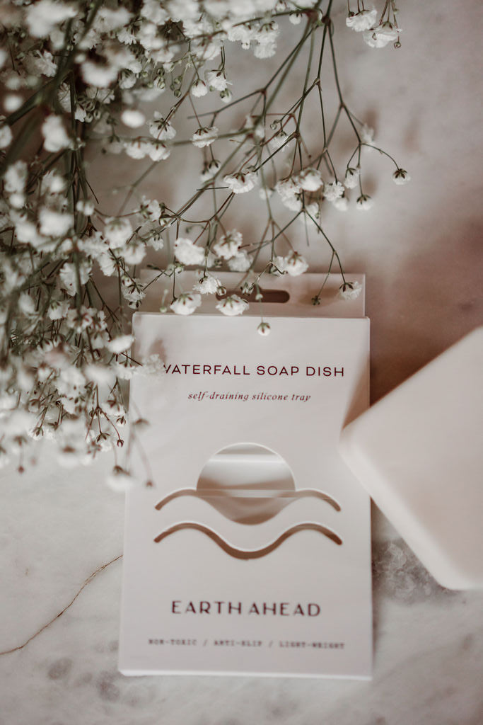 Earth Ahead soap dish with a bar of soap and white flowers on a marble surface