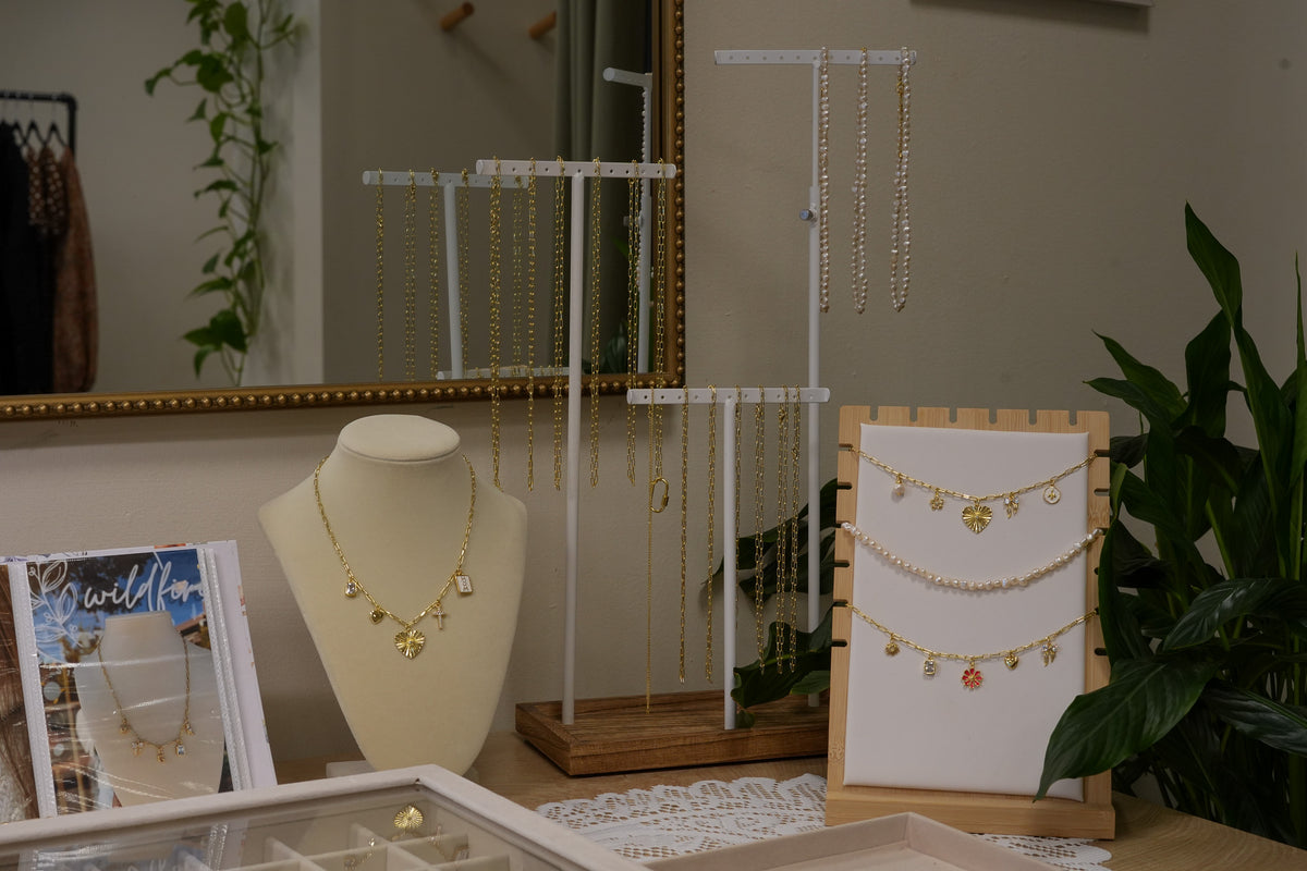 A collection of gold and pearl jewelry displayed on white jewelry stands, a cream-colored mannequin bust, and a wooden stand in a boutique setting.